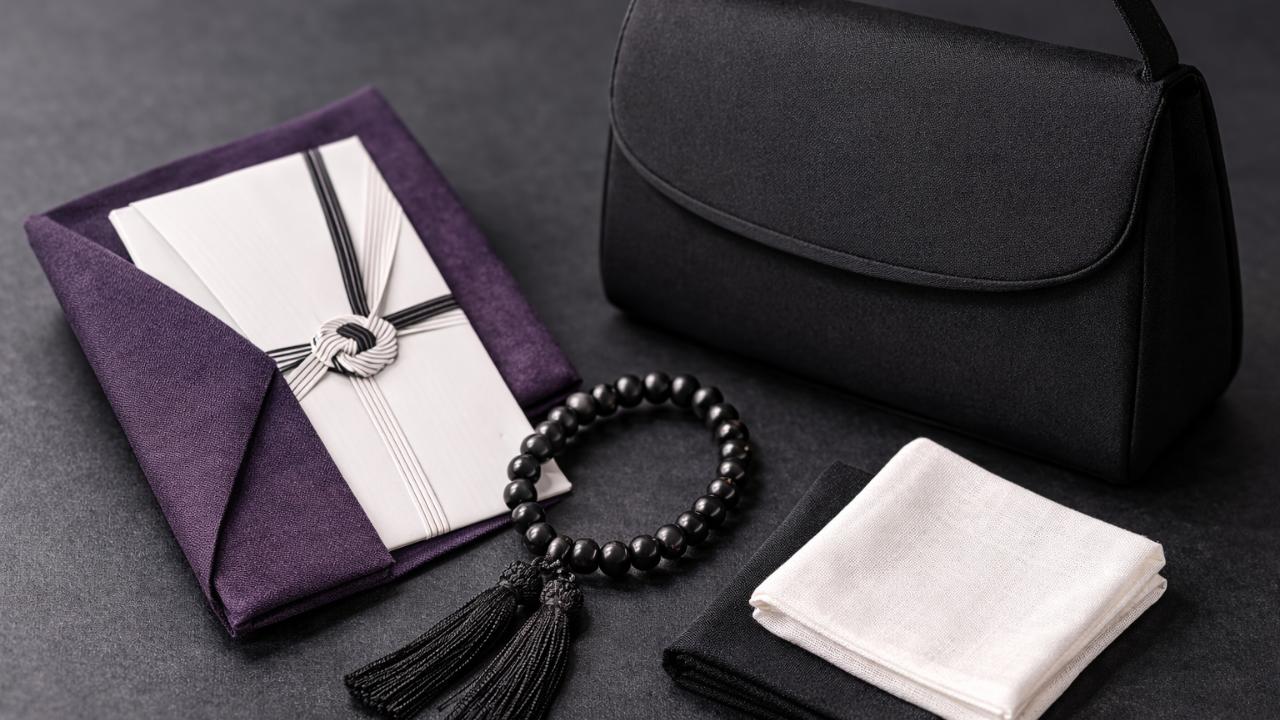 黒無地のフォーマルバッグ、紫またはグレーの袱紗に包んだ不祝儀袋、数珠、白または黒の無地ハンカチを、上品なダークグレーの背景の上に整然と配置