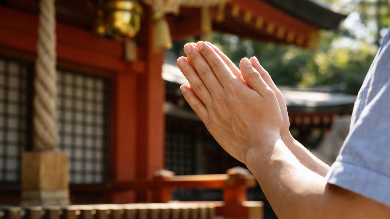 神社の拝殿前で胸の高さに手を合わせ、右指先を少し下にずらして二拍手前の所作をする手元のクローズアップ